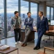 Tres arquitectos de diferentes edades y niveles de experiencia charlan amigablemente apoyados en un escritorio gerencial dentro de un moderno y lujoso estudio de arquitectura con ventanales y vista a la ciudad.